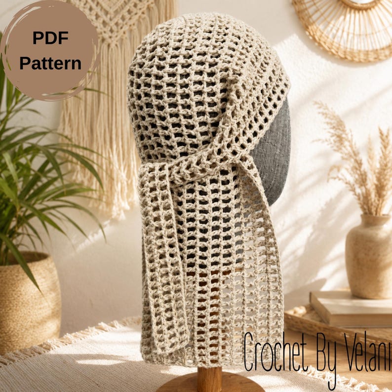 May include: A beige crochet head covering featuring an open grid pattern and a long, dangling side tie. The item is displayed on a dark gray mannequin head. A circular brown graphic in the upper left corner contains the text PDF Pattern.