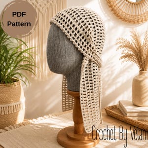 May include: A beige crochet headscarf featuring an open mesh pattern with two long side ties. The item is displayed on a gray mannequin head. The image includes text that reads PDF Pattern and Crochet By Velani in a script font style.