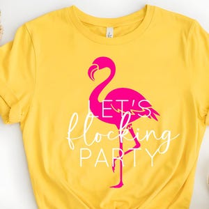 May include: Yellow t-shirt with a pink flamingo graphic. The flamingo has the words "LET'S flocking PARTY" in white script. The shirt is made of a soft material and has short sleeves.