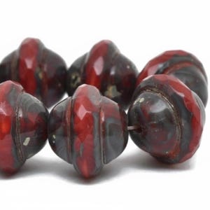 May include: Close-up of a strand of decorative beads. The beads are a deep red with streaks of black and gray. Each bead has a unique, rounded shape with a ridged texture. The beads are strung together, ready for crafting.