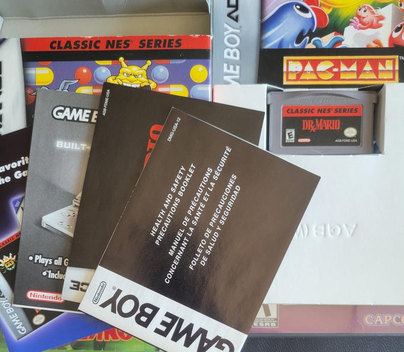 Op de afbeelding: Een verzameling Game Boy- en Classic NES Series-gamecartridges en handleidingen. De afbeelding toont een Dr. Mario-cartridge, een Pac-Man-gamebox en diverse instructieboekjes. Het Game Boy-logo is zichtbaar op de handleidingen.