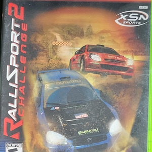 Puede incluir: Caja del juego RalliSport Challenge 2 para Xbox. La portada presenta dos coches de rally, uno rojo y otro azul, compitiendo en una pista de tierra. El juego está clasificado "E" para Todos e incluye el logotipo de Xbox Live.
