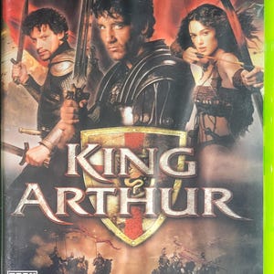 May include: King Arthur Xbox game case. The cover features three characters with swords, and a woman with a bow and arrow. The title "King Arthur" is prominently displayed, with a shield emblem. The game is rated "T" for Teen.