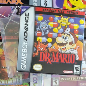 Op de afbeelding: Game Boy Advance game case voor "Dr. Mario" met het personage in een doktersjas, omringd door cartoonvirussen en pillen. De case zit in een beschermende plastic hoes, met het "Classic NES Series" logo zichtbaar.