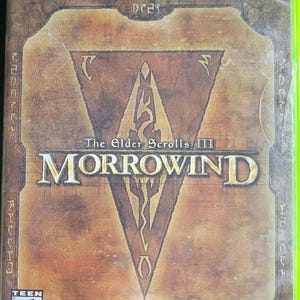 May include: Xbox game case for The Elder Scrolls III: Morrowind. The cover features a brown and tan design with a central triangular emblem and the game title in large, bold letters. The ESRB rating is visible in the lower left corner.
