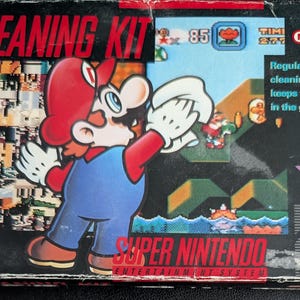 Könnte beinhalten: Super Nintendo Reinigungs-Kit-Box mit Mario in roter Mütze und blauer Latzhose. Das Box-Artwork zeigt eine Spielszene und den Text "Regelmäßige Reinigung hält dich im Spiel!"