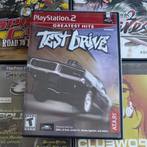 Op de afbeelding: Een PlayStation 2-gamecase voor "Test Drive" met een zwarte muscle car met een verhoogde voorkant. De gamecase is gelabeld "Greatest Hits" en bevat het Atari-logo. De game is door de ESRB beoordeeld als "Teen".