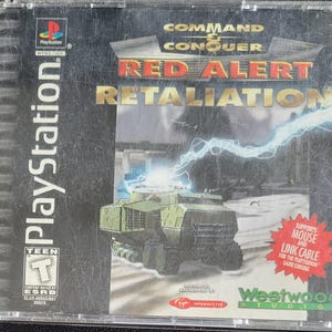 May include: A PlayStation game case for "Command & Conquer: Red Alert - Retaliation." The cover shows a green military vehicle, a lightning bolt, and the game's title in red and gold. The case is marked "Teen" by the ESRB.