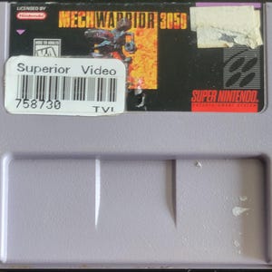 Peut inclure: Cartouche de jeu vidéo Super Nintendo pour MechWarrior 3050. La cartouche est violet clair avec une étiquette représentant un robot et le texte "MechWarrior 3050". Un autocollant "Superior Video" et un code-barres sont également visibles.