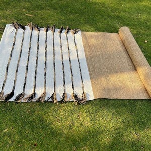 May include: A rectangular, woven rug with a white and black striped pattern on one end and a rolled-up tan section. The rug has decorative tassels on the striped end, suitable for indoor or outdoor use.