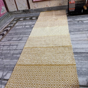 Puede incluir: Una alfombra larga y rectangular con un patr&oacute;n geom&eacute;trico. La alfombra presenta un degradado de colores, que va del beige claro al amarillo dorado. El dise&ntilde;o incluye formas de diamantes y &oacute;valos.