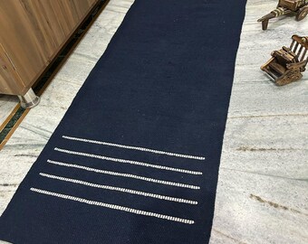 May include: A navy blue rectangular rug with white horizontal stripes at each end. The rug is made of a woven material and is placed on a marble floor. The rug is a decorative home accent.