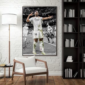 Könnte beinhalten: Gerahmtes Schwarz-Weiß-Foto eines Fußballspielers in weißer Uniform mit der Nummer 14, der auf dem Spielfeld jubelt. Das Foto enthält eine Unterschrift und die Worte "Emirates Fly Better".