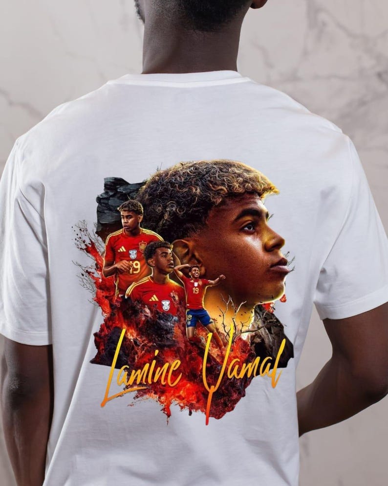 May include: White t-shirt with a graphic of a soccer player, featuring the name "Lamine Yamal" in orange script. The design includes images of the player in a red and yellow uniform, set against a fiery background.