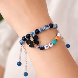 May include: A beaded bracelet with a black flower charm and a rhinestone centre. The bracelet includes blue and clear beads, silver chain accents, and beads spelling "HOPE".