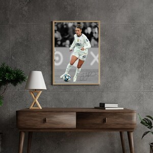 May include: A framed photograph of a soccer player in a white uniform with the number 20. The image is in black and white, with the player kicking a soccer ball. The frame is a light brown colour.
