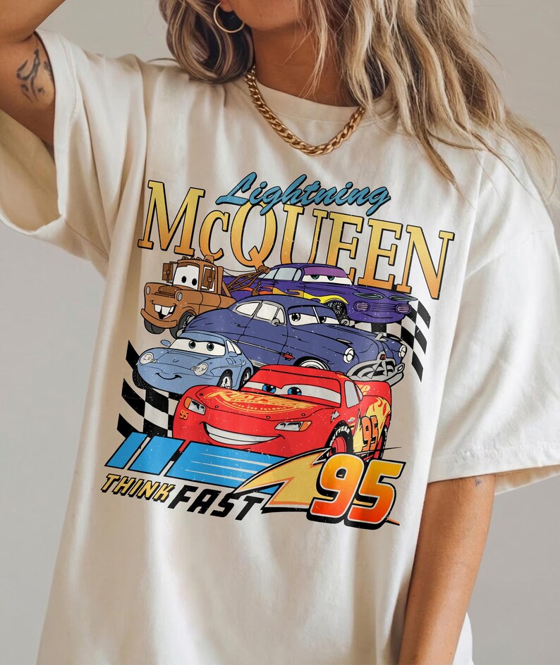 Puede incluir: Camiseta de color crema con un gr&aacute;fico de Rayo McQueen y otros personajes de la pel&iacute;cula Cars. El dise&ntilde;o incluye el texto "Lightning McQueen", "Think Fast" y el n&uacute;mero "95".
