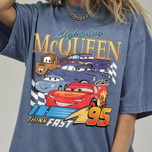 Puede incluir: Camiseta azul con un dise&ntilde;o de Rayo McQueen y otros personajes de Cars. El dise&ntilde;o incluye el texto "Lightning McQueen", "Think Fast" y el n&uacute;mero "95". La camiseta tiene un aspecto vintage y desgastado.