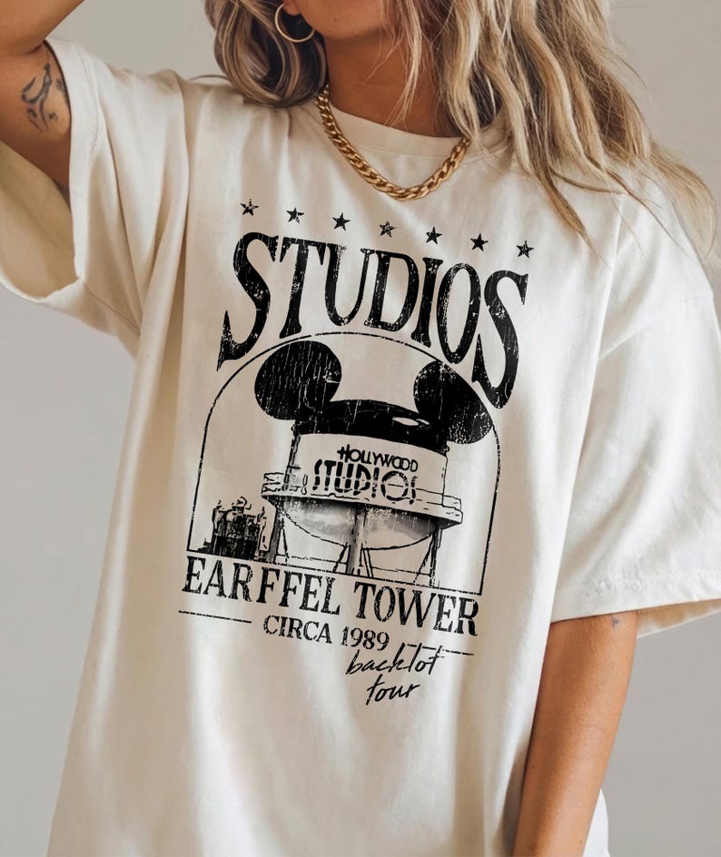 May include: Cream-colored t-shirt featuring a black graphic of the Hollywood Studios Earffel Tower with Mickey Mouse ears, the word "STUDIOS" above, and "EARFFEL TOWER CIRCA 1989 backlot tour" below.