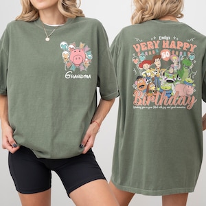 May include: Olive green t-shirt with a graphic of a pink pig and the word "Grandma" on the front. The back features a "Very Happy Birthday" design with cartoon characters and the number 50. The text "Wishing you a year filled with joy and good memories" is also included.