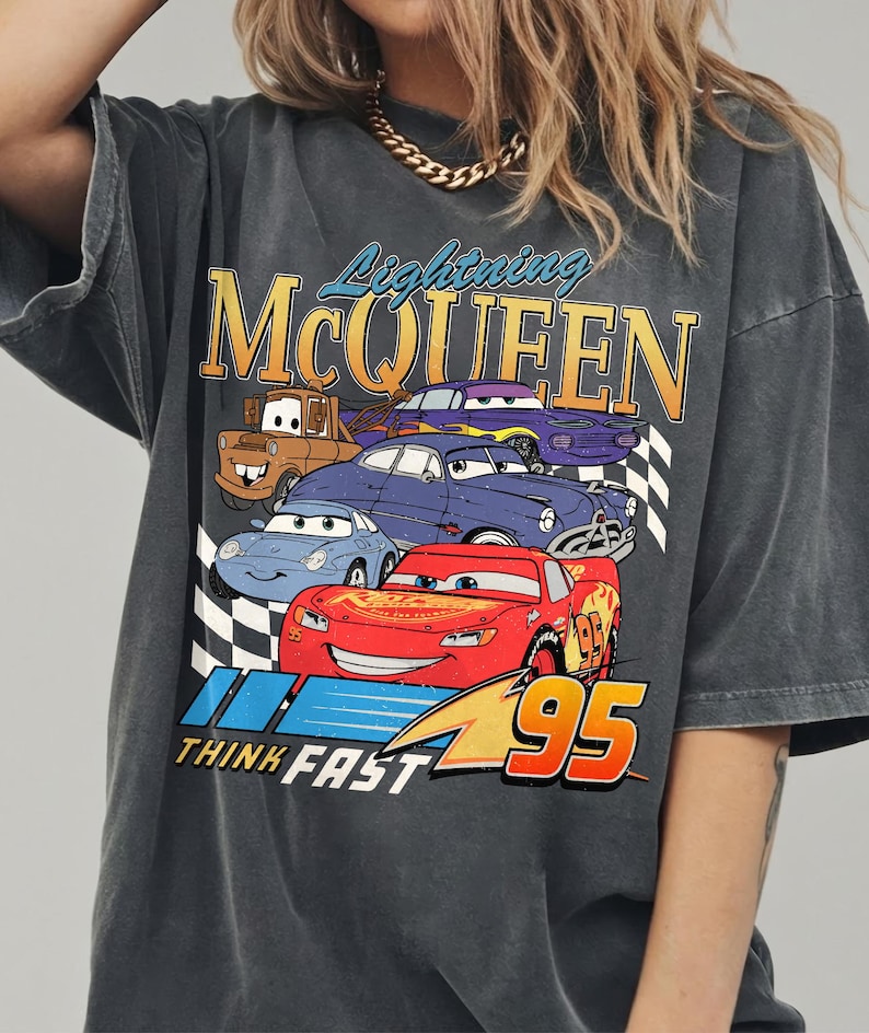 Puede incluir: Camiseta gris oscuro con un gr&aacute;fico de Rayo McQueen y otros personajes de la pel&iacute;cula Cars. El dise&ntilde;o incluye el texto "Lightning McQueen", "Think Fast" y el n&uacute;mero "95".