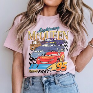 Puede incluir: Camiseta rosa claro con un dise&ntilde;o de Rayo McQueen y otros personajes de Cars. El dise&ntilde;o incluye el texto "Lightning McQueen" y "Think Fast" con el n&uacute;mero 95. La camiseta la lleva una persona.
