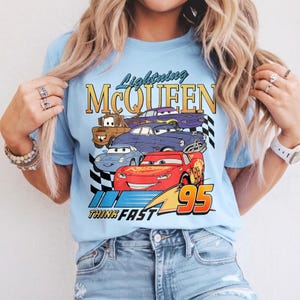 Puede incluir: Camiseta azul claro con un gr&aacute;fico de Rayo McQueen y otros personajes de Cars. El dise&ntilde;o incluye el texto "Lightning McQueen" y "Think Fast 95" en un estilo retro. La camiseta est&aacute; hecha de un material suave.