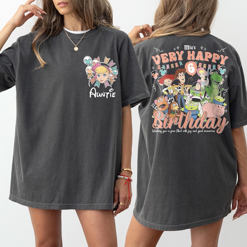 May include: Dark gray t-shirt with a graphic of a cartoon character and the word "Auntie" on the front. The back of the shirt features a "Toy Story" themed birthday design with the words "Very Happy Birthday".