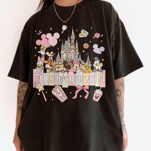 Puede incluir: Camiseta negra con un gr&aacute;fico colorido de Disneyworld. El dise&ntilde;o incluye un castillo, Mickey Mouse, Minnie Mouse, Donald Duck y otros personajes. La palabra "Disneyworld" se muestra en colores pastel.