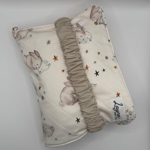 May include: A quilted pouch in cream fabric featuring a repeating pattern of brown bunnies and small stars. A beige elasticized strap runs vertically across the center. A white rectangular label with the black text Layne Quilt Co is attached.