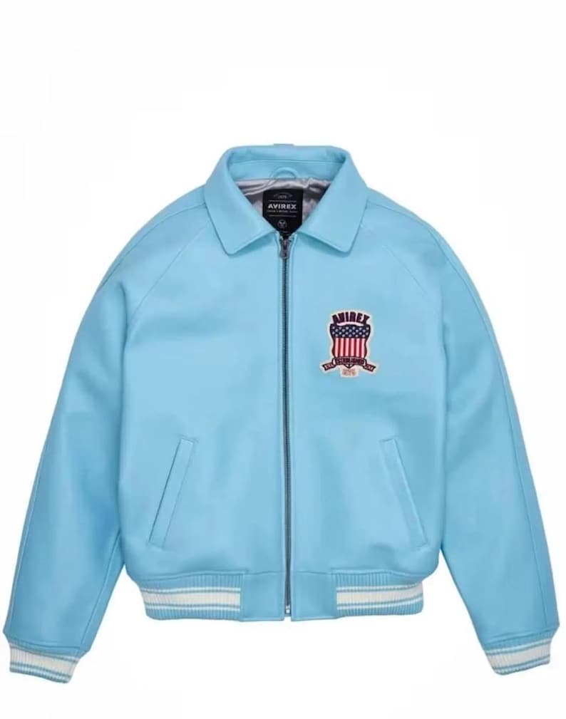 Puede incluir: Chaqueta azul claro con cierre de cremallera, cuello y bolsillos laterales. Los pu&ntilde;os y el dobladillo tienen un ribete a rayas blanco y azul claro. Un emblema con la palabra "AVIREX" y un dise&ntilde;o rojo, blanco y azul est&aacute; en el pecho.