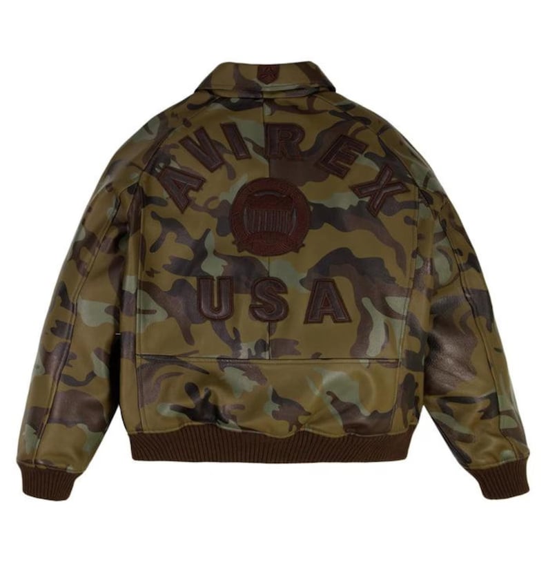 Pu&ograve; includere: Giacca in pelle con motivo mimetico con la scritta "AVIREX USA" sul retro. La giacca presenta colletto, polsini e orlo marroni e un'emblema marrone sopra il testo "USA". Il motivo mimetico utilizza tonalit&agrave; di verde, marrone e beige.
