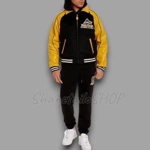 May include: Black and yellow varsity jacket with the "AVIREX" logo on the chest. The jacket has a black hood and is paired with black sweatpants and white sneakers. The outfit is a complete set.