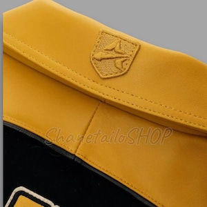 May include: Close-up of a yellow leather accessory with a stitched emblem. The accessory has a black interior and a contrasting white trim. The text "Sharetailo SHOP" is visible.