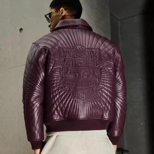 Pu&ograve; includere: Giacca bomber in pelle bordeaux con design trapuntato. La parte posteriore della giacca presenta un'emblema in rilievo con la scritta "Vibe 50". La giacca ha orlo e polsini a coste.