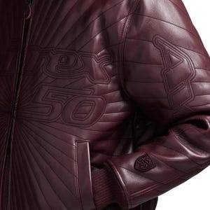 Pu&ograve; includere: Giacca in pelle bordeaux con cuciture trapuntate e polsino a coste. La giacca presenta la scritta "Racer 50" cucita sul davanti e un logo sulla manica. Il design include una chiusura a zip e una tasca.