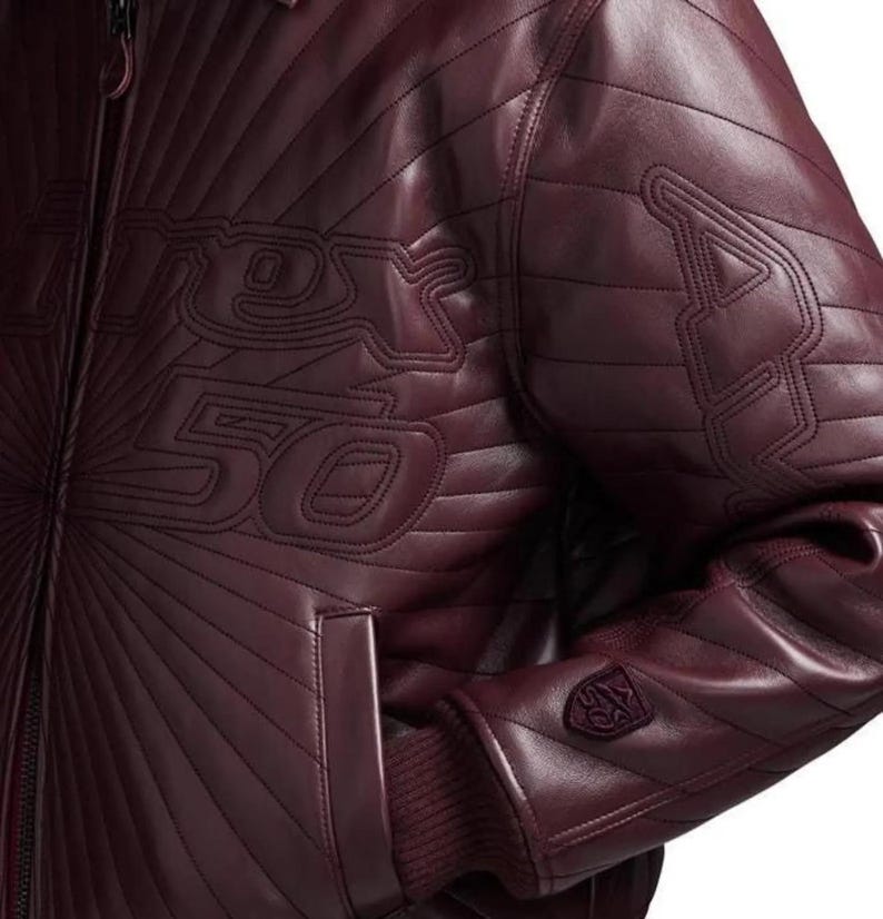 Pu&ograve; includere: Giacca in pelle bordeaux con cuciture trapuntate e polsino a coste. La giacca presenta la scritta "Racer 50" cucita sul davanti e un logo sulla manica. Il design include una chiusura a zip e una tasca.