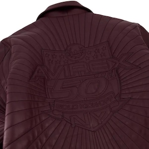 Pu&ograve; includere: Giacca in pelle bordeaux con dettagli cuciti. La schiena presenta un emblema ricamato con la scritta "AVIREX 50TH GOLD KICK-OFF NY" e dettagli a stella e corona. La giacca ha un collo.