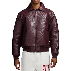 Pu&ograve; includere: Giacca in pelle bordeaux con zip e orlo e polsini a coste. La giacca presenta testo in rilievo sul petto e sulle maniche. La giacca &egrave; abbinata a pantaloni della tuta bianchi.