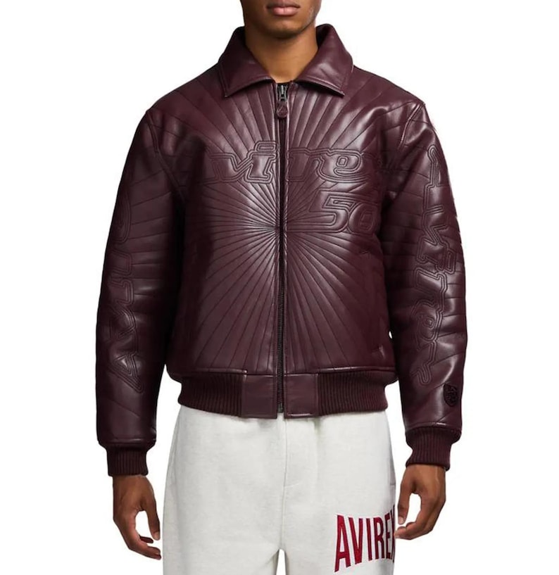 Pu&ograve; includere: Giacca in pelle bordeaux con zip e orlo e polsini a coste. La giacca presenta testo in rilievo sul petto e sulle maniche. La giacca &egrave; abbinata a pantaloni della tuta bianchi.