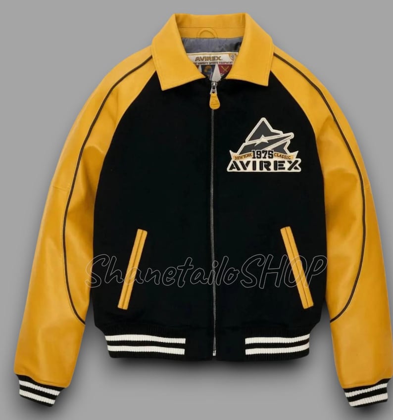 May include: Black and yellow varsity jacket with a zip-up front. The jacket features yellow sleeves and collar, with black on the body. It has a white and black striped hem and cuffs. The jacket has the text "AVIREX" and "1975 Classic" on the chest.