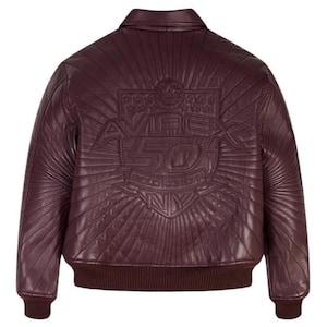 Pu&ograve; includere: Giacca bomber in pelle bordeaux con colletto, polsini e orlo a coste. La schiena presenta un design in rilievo con la scritta "AVIREX 50 GOLD KICKER NY" e un motivo a raggi solari. La giacca ha una classica silhouette bomber.