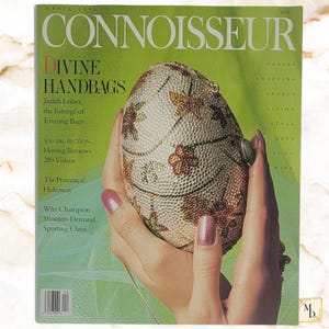 Op de afbeelding: Het aprilnummer van 1990 van het tijdschrift Connoisseur heeft een groene omslag met de tekst Divine Handbags en Judith Leiber, the Fabergé of Evening Bags. Een eivormige, met kristallen ingelegde clutch met bloemmotief staat centraal.