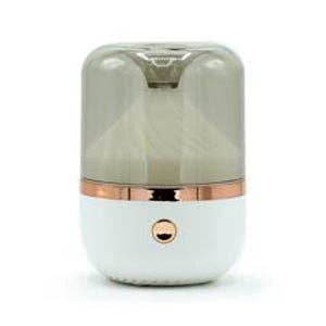 Puede incluir: Difusor de aceites esenciales blanco y oro rosa con una parte superior gris ahumado transparente. El difusor tiene forma cilíndrica con una banda de oro rosa y un solo botón dorado. El interior presenta un diseño blanco en forma de cono.