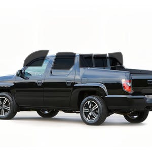 May include: Black pickup truck with tinted windows and silver and black alloy wheels. The truck has a covered bed and is set against a white background. The vehicle is a four-door model.