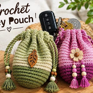 May include: Two crochet key pouches with drawstring closures. One is sage green with a wooden leaf charm, the other is a pink and purple gradient with a wooden flower charm. Both feature braided cords with wooden beads and tassels at the ends.