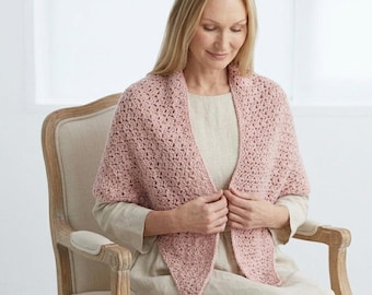 May include: A light pink crocheted shawl with a textured pattern. The shawl is draped over the shoulders and has a triangular shape in the front. The woman is sitting in a beige chair.