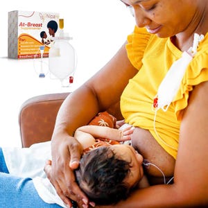 May include: An image of a woman breastfeeding a baby while using an At-Breast Supplementer. The supplementer includes a bag, tubing, and a box with the product name and logo. The baby is wearing a patterned onesie.
