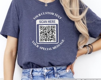 May include: Navy blue t-shirt with a white QR code design. The text around the QR code says "YOUR CUSTOM TEXT", "SCAN HERE", and "YOUR SPECIAL MESSAGE". The shirt is worn by a person.