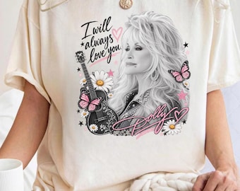 Puede incluir: Una camiseta de color crema con un estampado gráfico de una mujer rubia, una guitarra acústica negra, margaritas blancas, mariposas rosas y estrellas. El texto dice I will always love you y Dolly en letra cursiva.